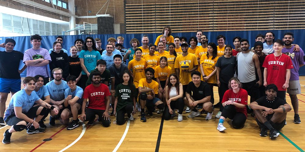 Group of students wearing different colour t-shirts standing on the Curtin indoor basketball courts. 