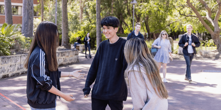 Three students standing outdoors talking to each other.