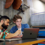 Two students helping eachother at a laptop and studying together