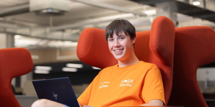 Kai smiles at camera while sitting down with his computer.