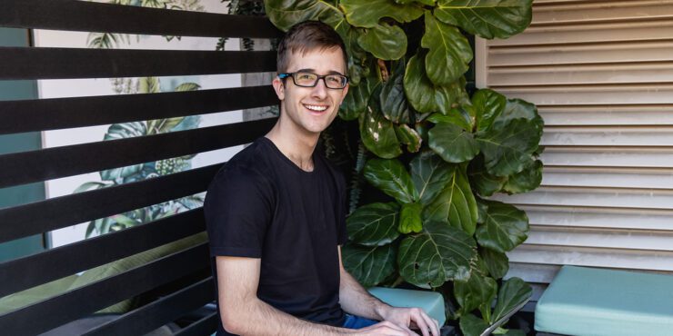 A student is sitting on a bench with his laptop.