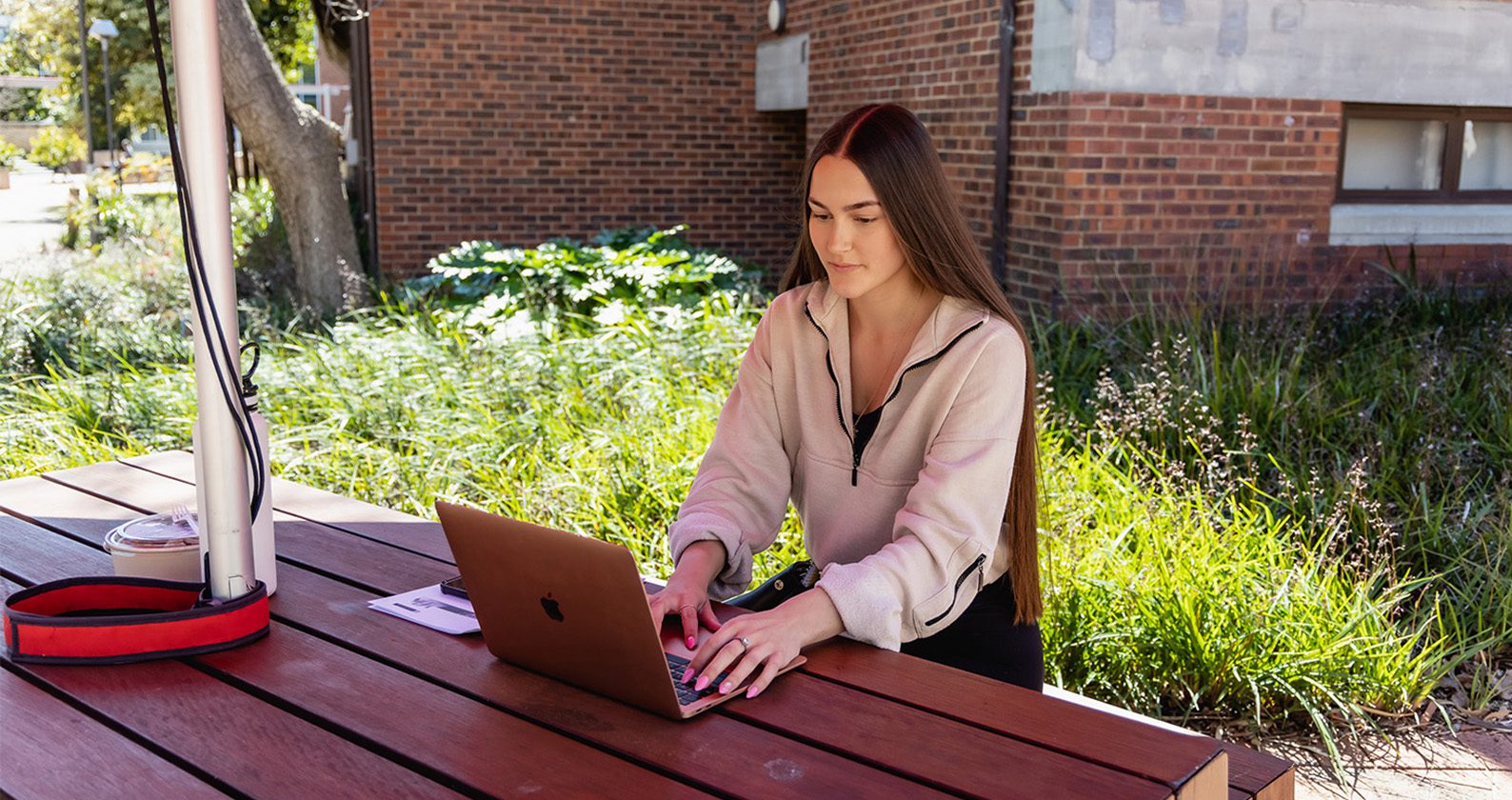 A female student sitting at an outdoor table and working on a laptop