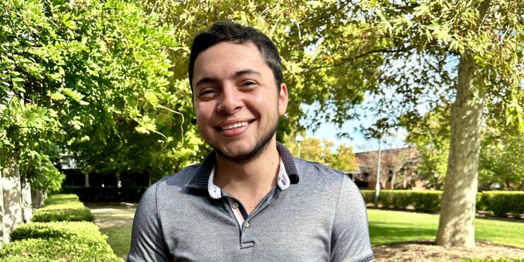 Carlos smiles at the camera with lush campus gardens behind him.