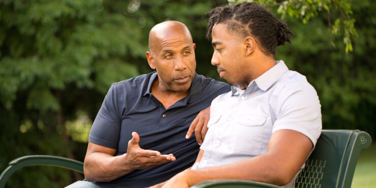 Father and son sitting on a garden bench. Father is giving his son some advice.