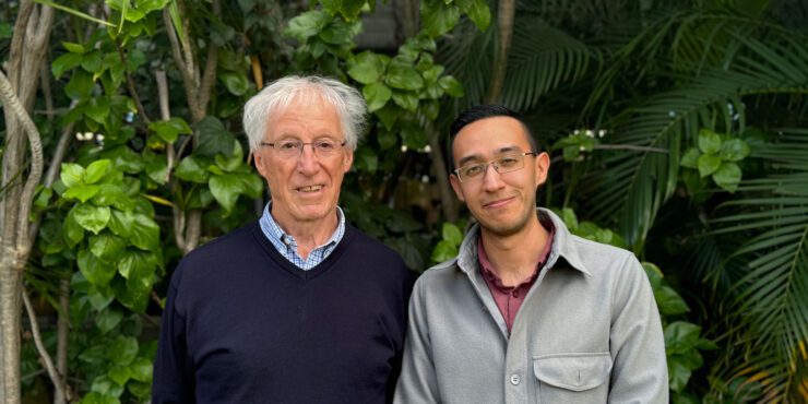 David and Bruno smile at the camera. They stand in front of a wall of plants.