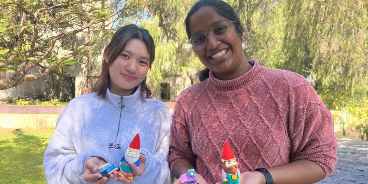 Two students stand outdoors holding painted gnomes.