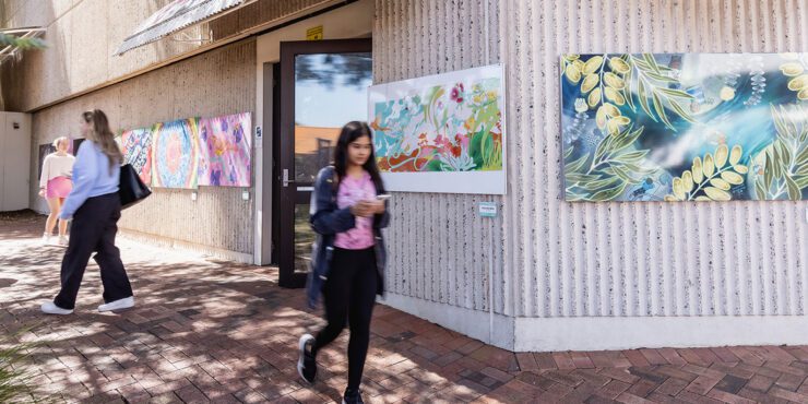 Students walking outside a building with art on the walls.