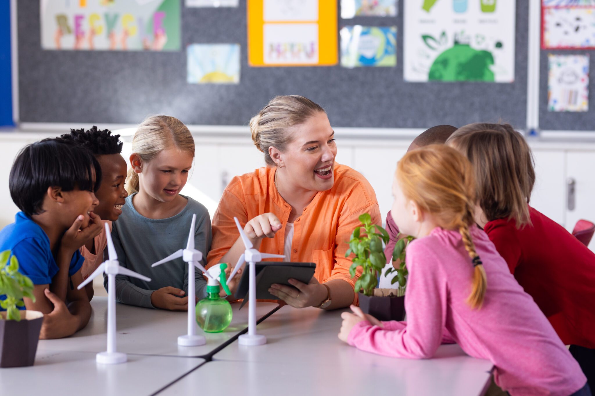 In school, female teacher with tablet, engaging diverse students with wind turbines and plants