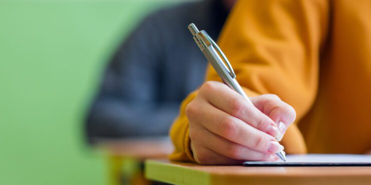Student taking exam in classroom. Education test and literacy concept. Cropped shot, hand detail.