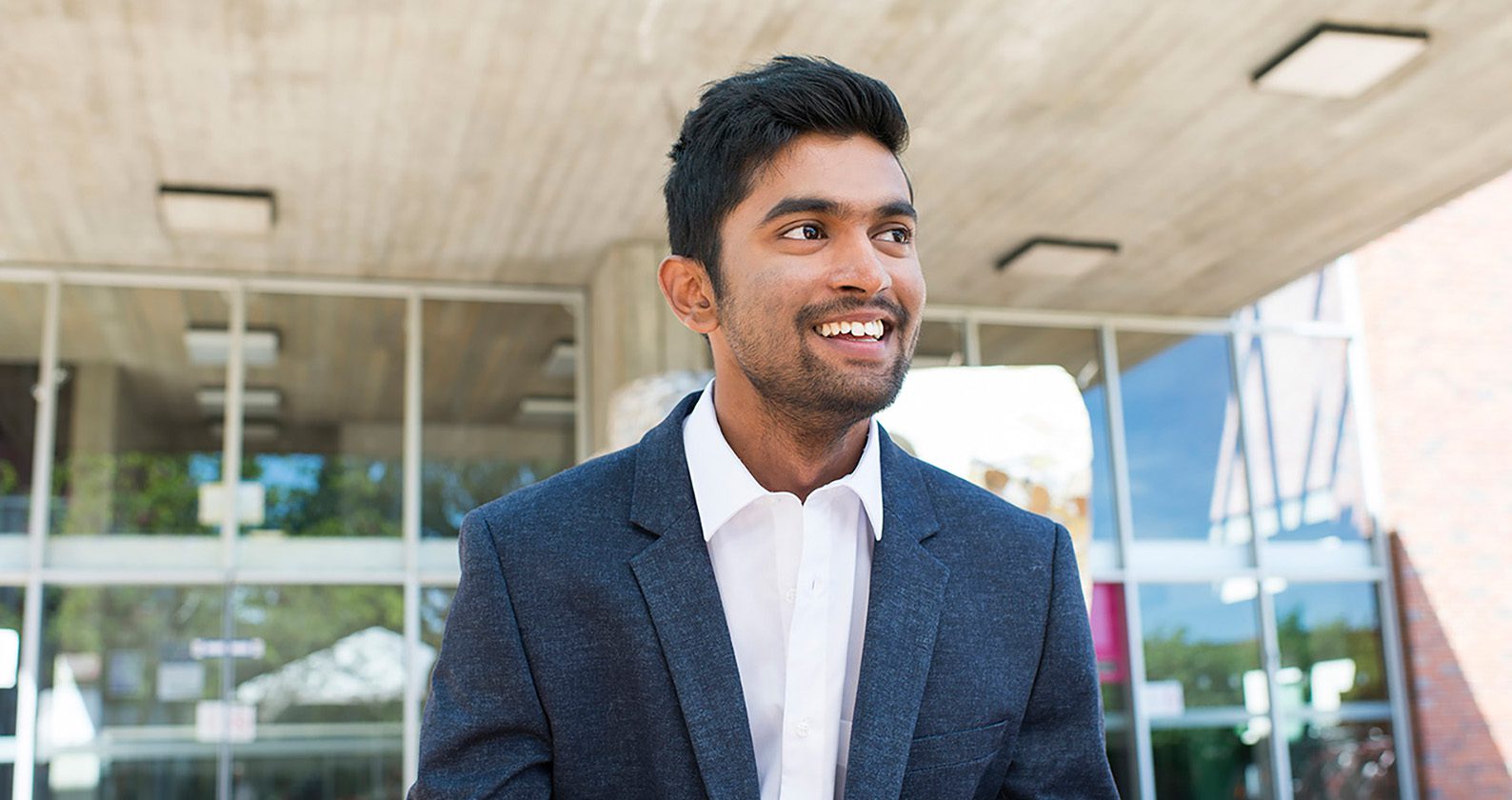 A male student wearing a suit and smiling while looking off into the distance.