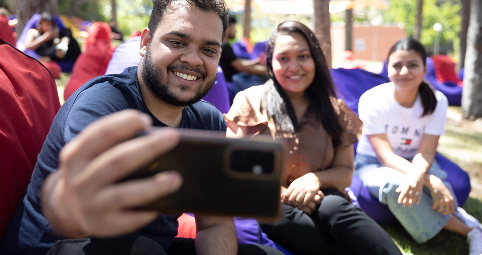 A male student taking a selfie on his phone with two female friends