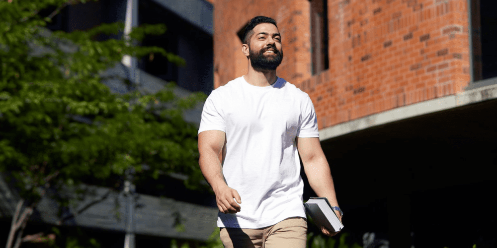 Male Curtin University student walking, with the Curtin Bentley campus in the background.