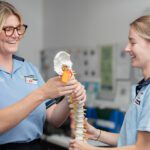 Two students smiling and holding a replica spine.