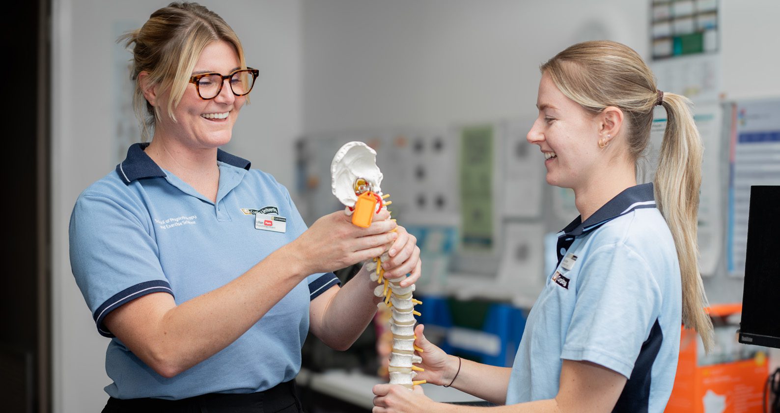 Two students smiling and holding a replica spine.