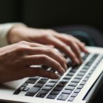 Persons hands typing on a laptop.