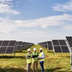 Three people in hi-vis standing in a field of solar panels.