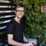 A student smiling at the camera while sitting on a bench.