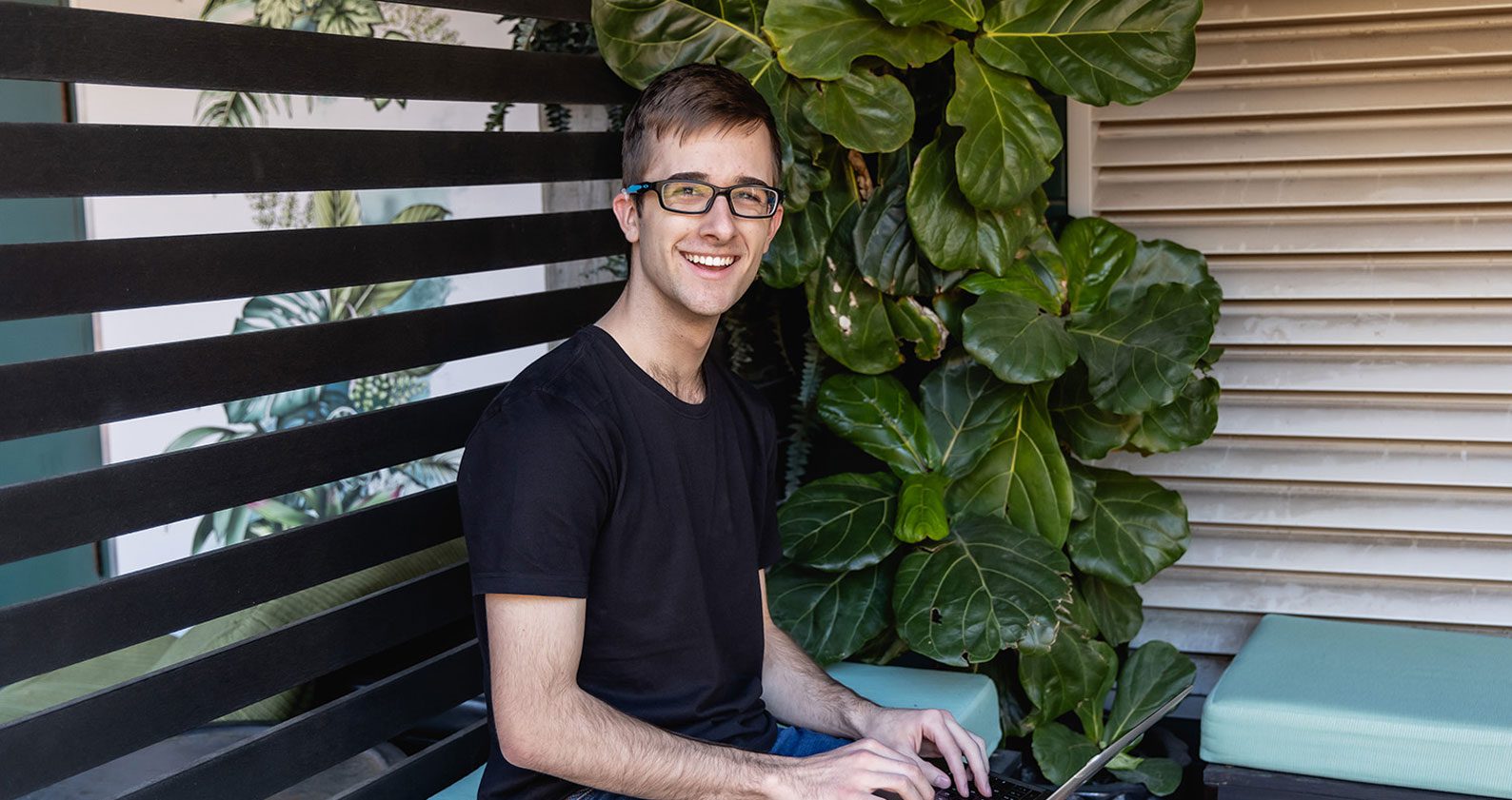 A student smiling at the camera while sitting on a bench.