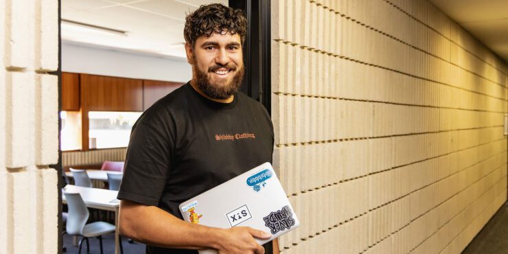 A student holding a laptop and smiling at the camera