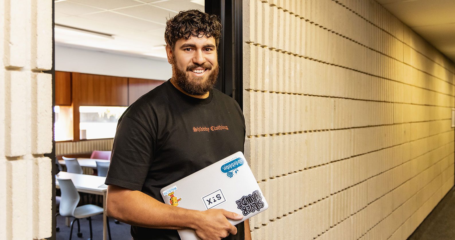 A student holding a laptop and smiling at the camera