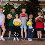 Children smiling holding sporting equipment.