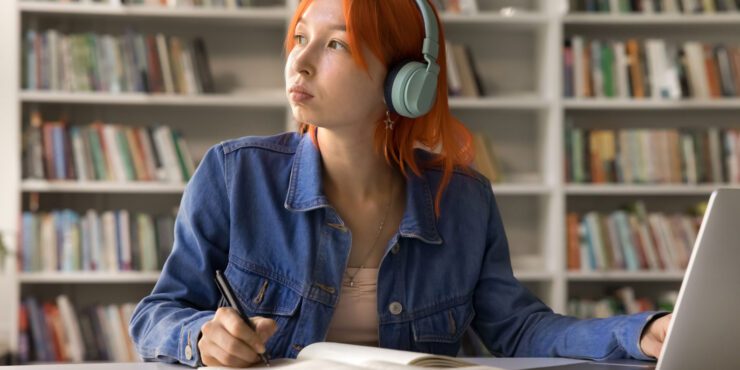 Student looking off into the distance wearing headphones while sitting at a desk with a laptop.