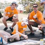Four students helping paint white lines on a road.