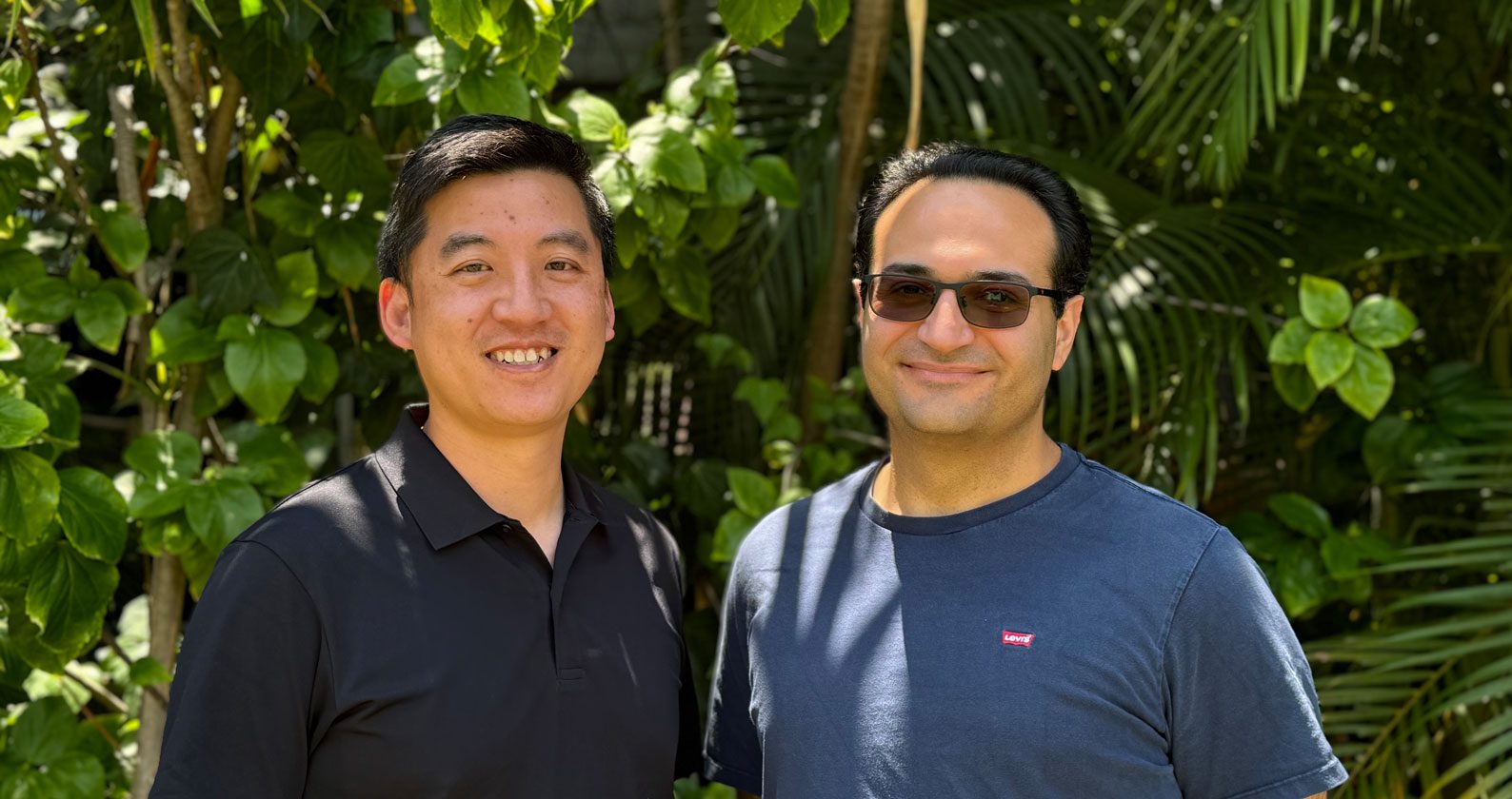 Shih Ching and Arash posing in front of a wall of greenery.