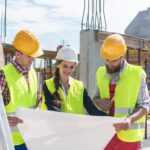 Female construction worker analysing a blueprint with two male workers outdoors on the construction site.