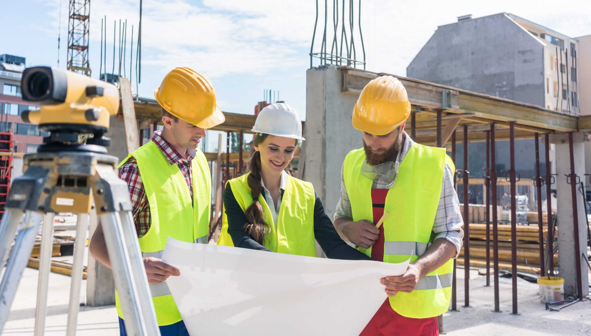Female construction worker analysing a blueprint with two male workers outdoors on the construction site.