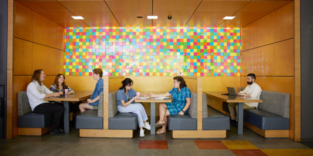 Students sit and chat in booth seating along a colourful tiled wall.