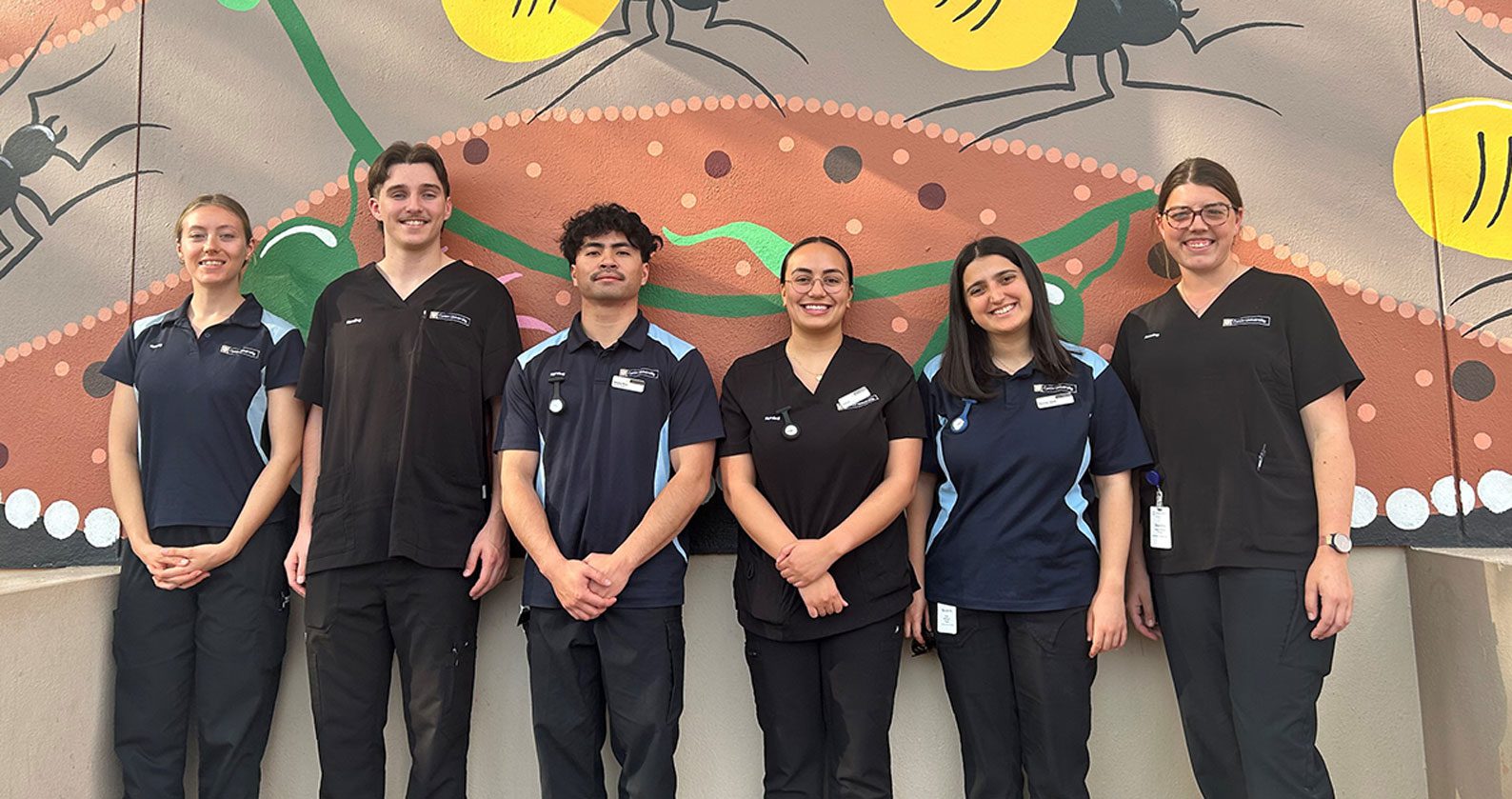 A group of rural placement students stand in a line smiling at the camera.