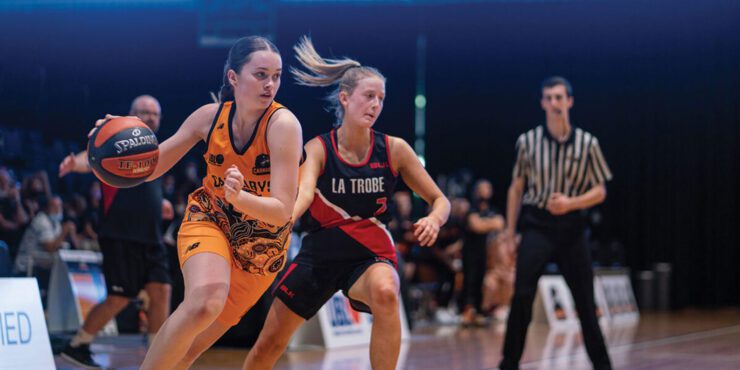 Two students playing basketball run across the court.