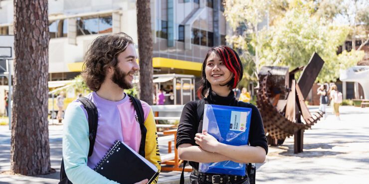 Two students holding books and smiling at each other.