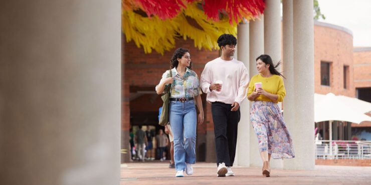 Three students walking together and holding coffee.