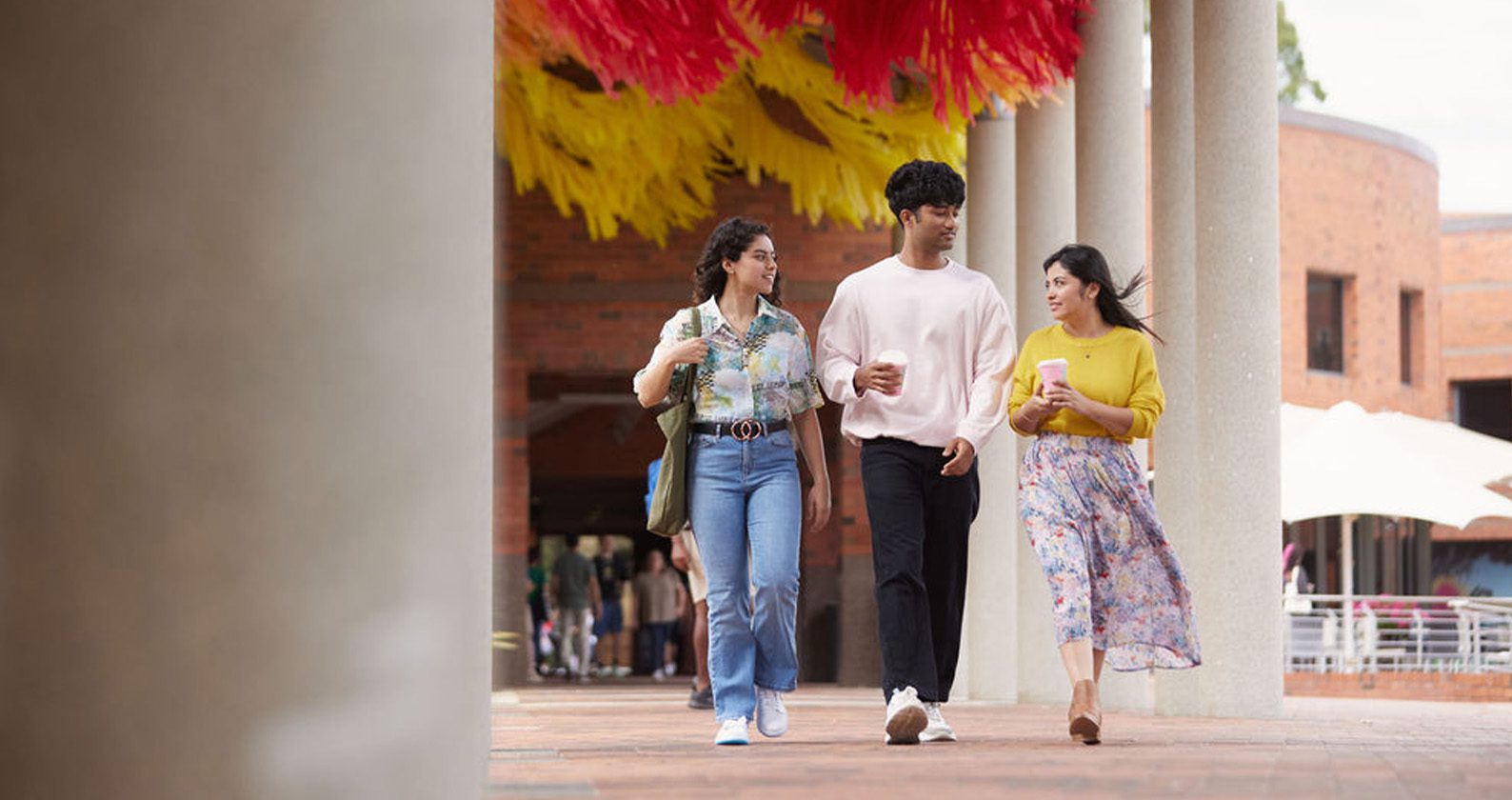 Three students walking together and holding coffee.