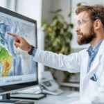 A scientist wearing safety glasses points at a digital map on a monitor.