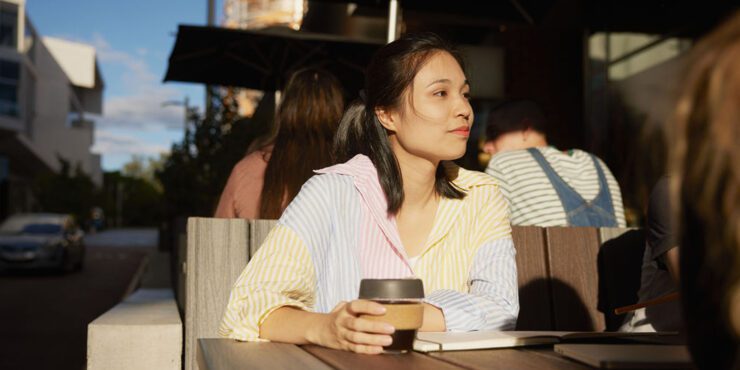 A student sitting and holding a coffee keep cup.