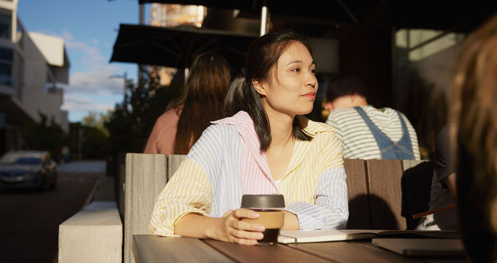 A student sitting and holding a coffee keep cup.