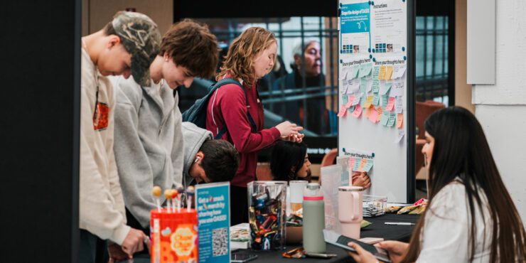 A group of students standing at a table with snacks, pens and informational materials.