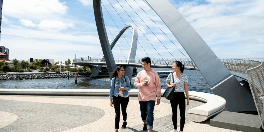 Three students walking and talking across Elizabeth Quay’s pedestrian bridge in Perth on a sunny day.