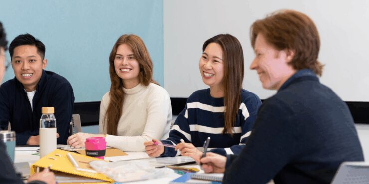 Group of university students sitting around a table, smiling and talking during a collaborative class activity.
