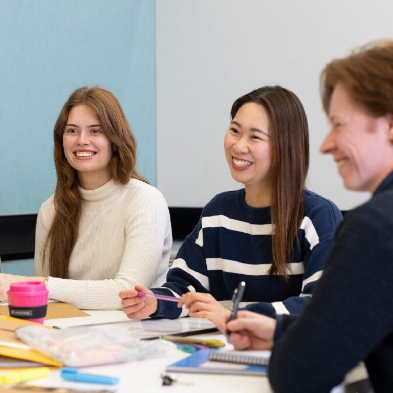 Group of university students sitting around a table, smiling and talking during a collaborative class activity.