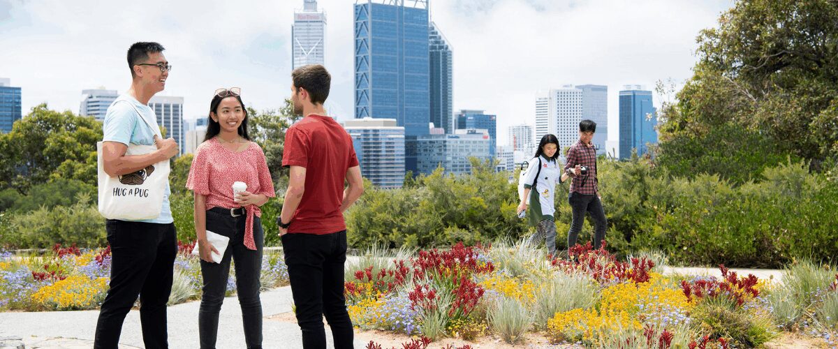 Group of students talking and walking through a colourful garden with Perth city skyline in the background.
