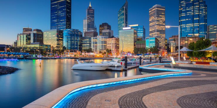 Perth city skyline at dusk, with high-rise buildings lit up and reflections on the water at Elizabeth Quay.