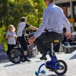 Person riding a small bike with training wheels at an outdoor event.