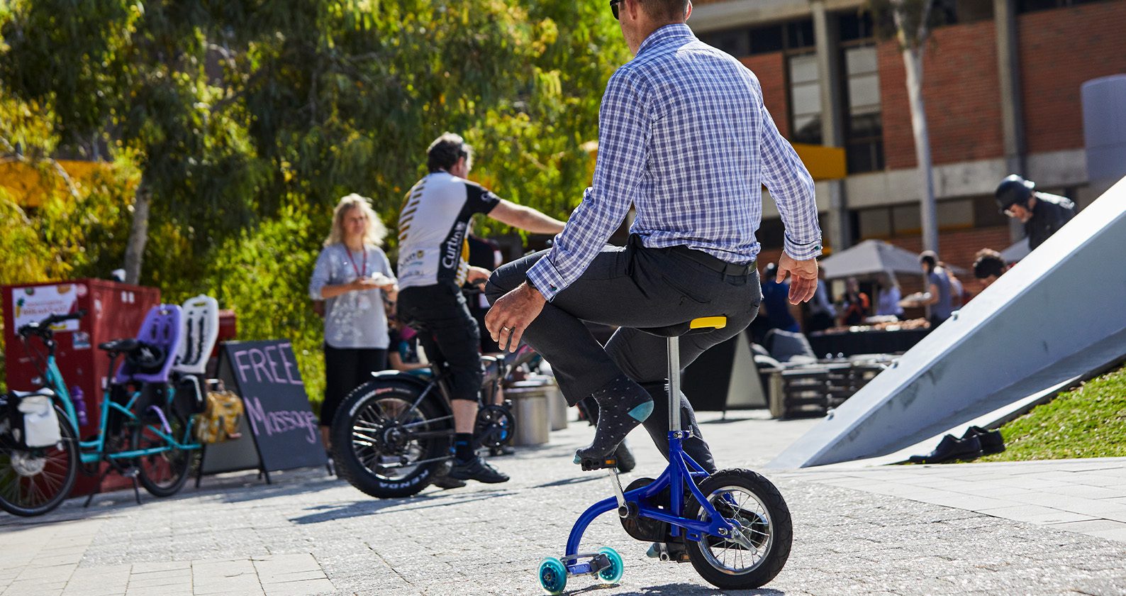 Person riding a small bike with training wheels at an outdoor event.