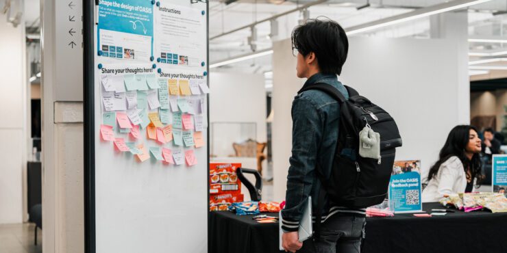Person at a feedback hub with sticky notes, snacks and info tables.