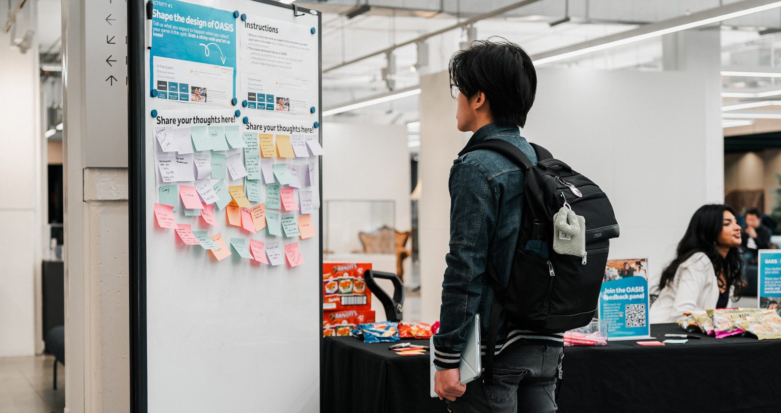 Person at a feedback hub with sticky notes, snacks and info tables.