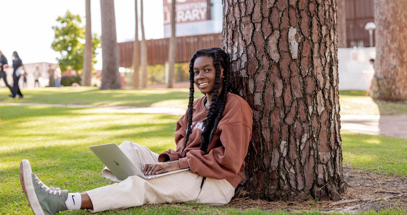 Person using a laptop under a tree near a library.